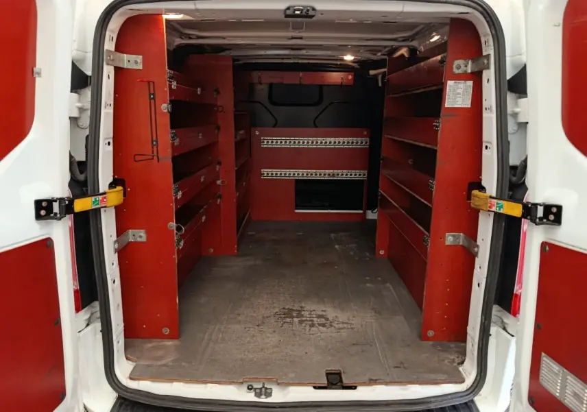 Vue arrière du Ford Transit Custom blanc de 2020, montrant l’intérieur utilitaire avec étagères rouges et cloison pleine noire.