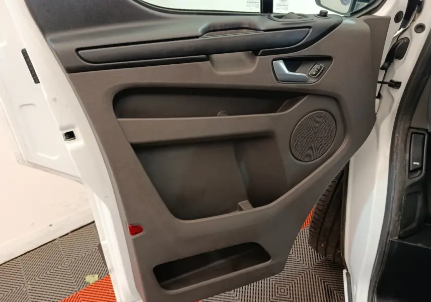Vue intérieure côté gauche de la porte avant blanche du Ford Transit Custom avec panneau noir et haut-parleur intégré.