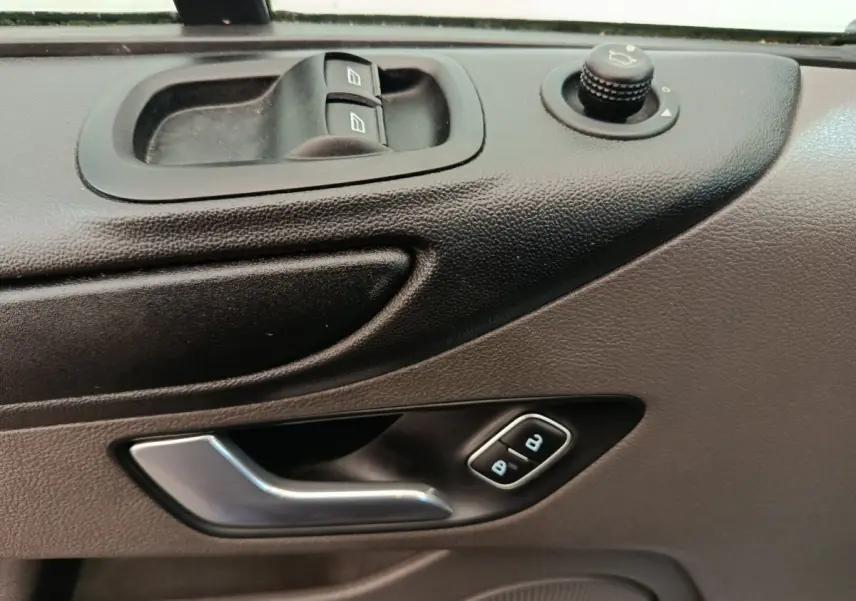 Gros plan sur la porte côté conducteur du Ford Transit Custom blanc, montrant les commandes des vitres et la poignée argentée.