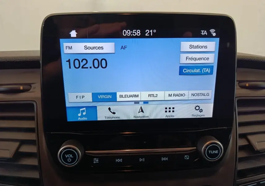 Écran tactile central du Ford Transit Custom blanc, affichant la radio FM à 102.00 MHz en intérieur véhicule.