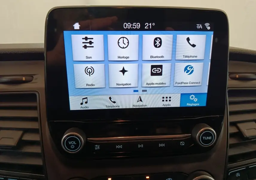 Écran tactile central du Ford Transit Custom blanc, affichant les options multimédia et réglages, vue intérieure frontale.