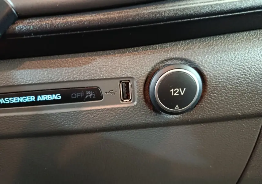 Détail intérieur du tableau de bord du Ford Transit Custom, prise 12V et port USB visibles sur plastique noir texturé.