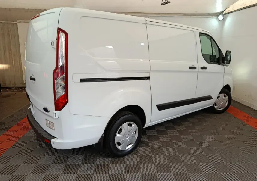 Ford Transit Custom blanc vu en 3/4 arrière droit dans un garage avec protections latérales noires et jantes acier.