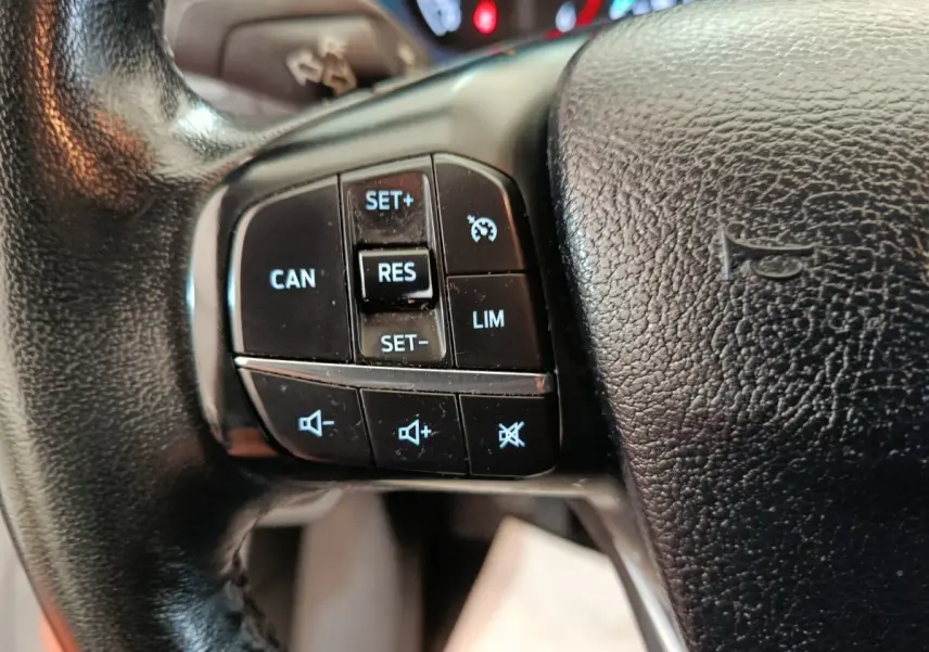 Gros plan sur les commandes de régulateur de vitesse et volume au volant cuir noir du Ford Transit Custom Fourgon blanc.