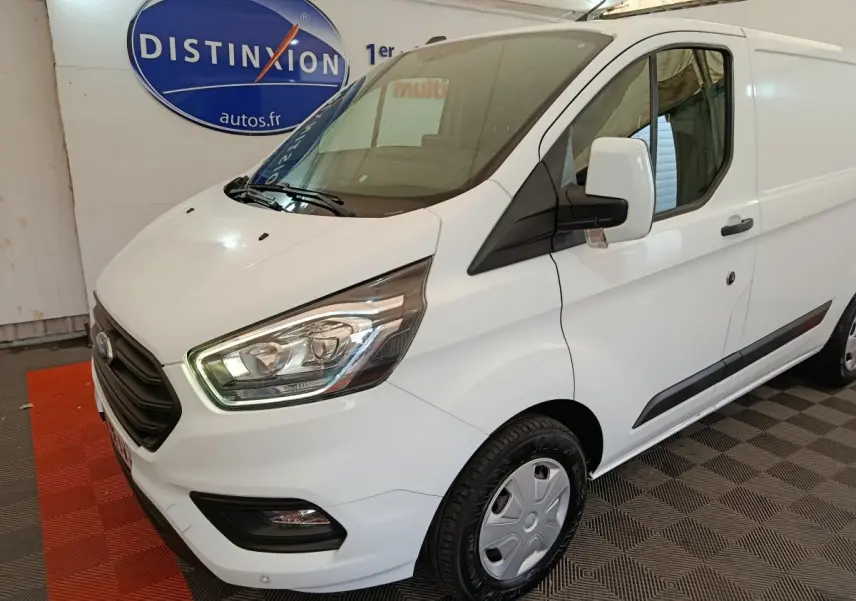 Vue 3/4 avant droit d'un fourgon Ford Transit Custom blanc avec phares allumés et jantes acier.