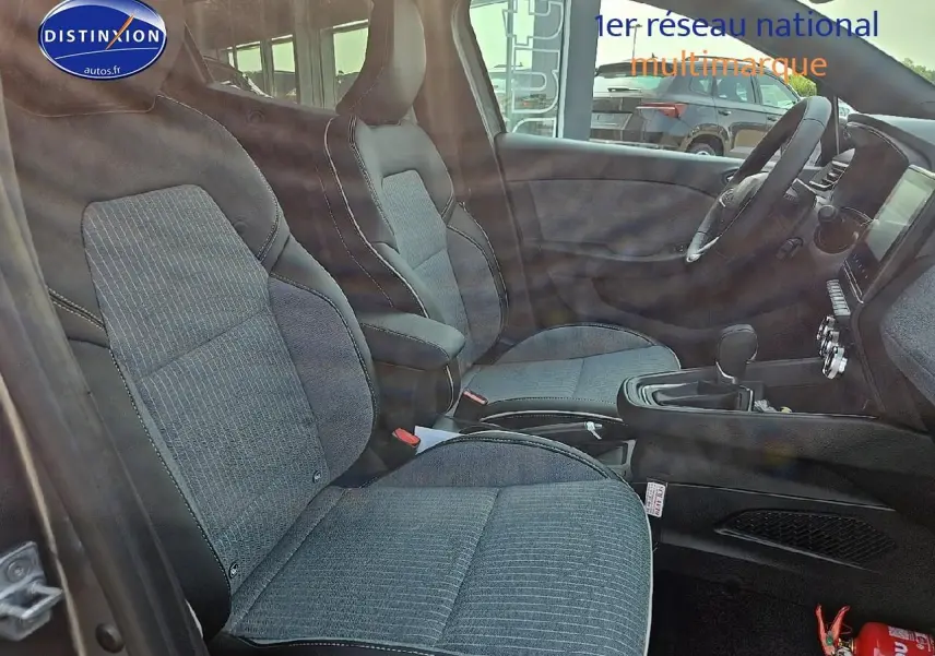 Vue intérieure côté conducteur de la Renault Clio V 1.0 TCe 90 Techno avec sièges tissu gris et accoudoir central.