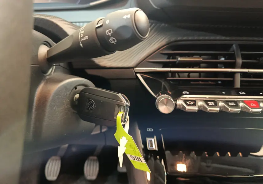 Gros plan sur le tableau de bord noir et la clé insérée dans le contacteur d'une Peugeot 208 gris foncé, version PureTech 100 S&S Allure.