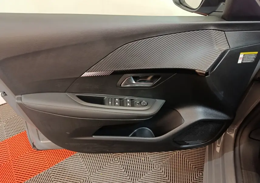 Porte côté conducteur gris foncé de la Peugeot 208 PureTech 100 S&S Allure 2025 avec commandes électriques et insert effet carbone.