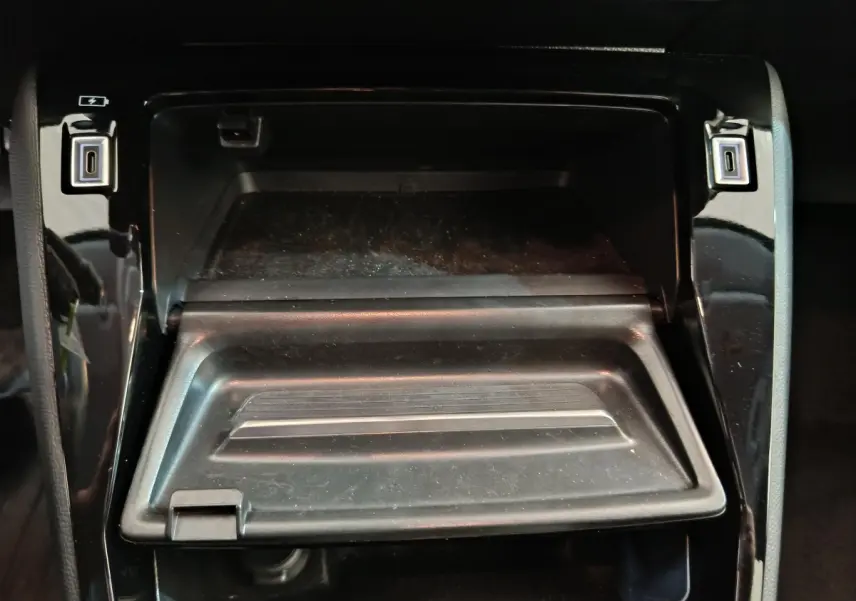 Rangement central ouvert avec ports USB visibles sur la console noire brillante d'une Peugeot 208 2025 gris foncé.
