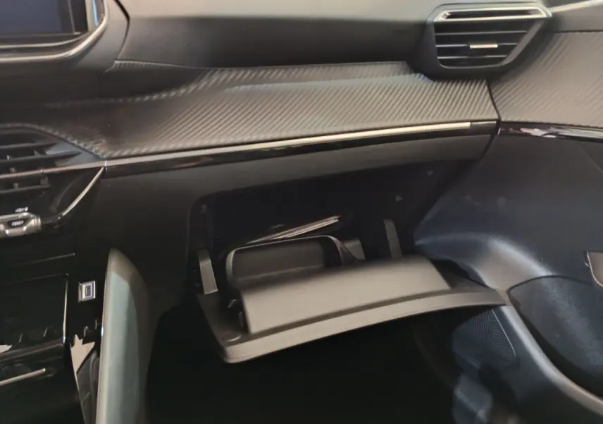 Intérieur de la Peugeot 208 PureTech 100 S&S Allure 2025, vue sur la boîte à gants ouverte et tableau de bord noir.