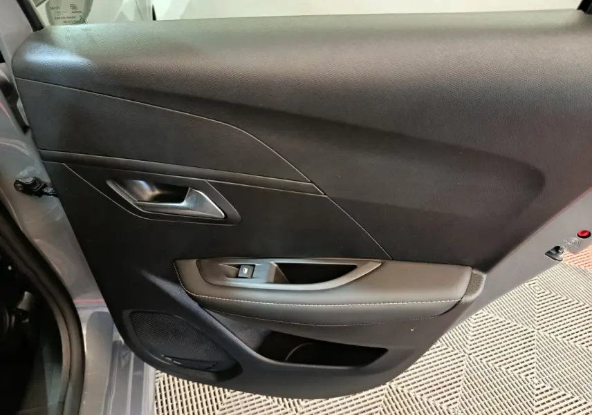 Vue intérieure côté gauche de la porte avant gris foncé de la Peugeot 208 PureTech 100 S&S Allure avec poignée et commande de vitre.