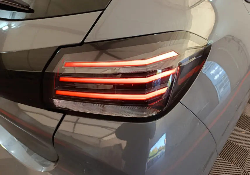 Feu arrière droit allumé sur Peugeot 208 gris foncé, vue rapprochée du coin arrière du véhicule.