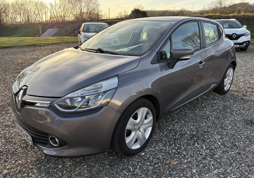 Renault Clio IV gris vue 3/4 avant droit sur parking gravillonné, avec jantes alliage et phares distinctifs.