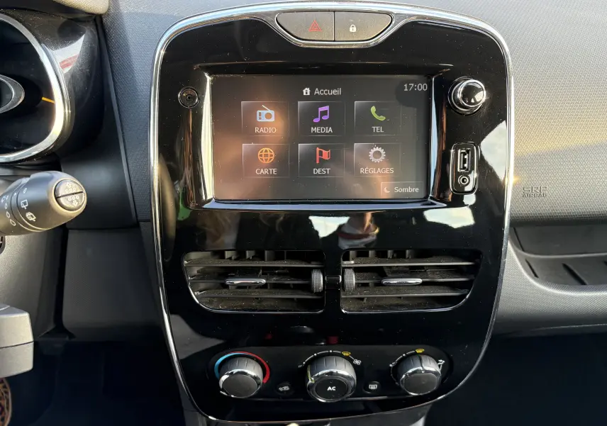 Vue rapprochée du tableau de bord noir brillant de la Renault Clio IV gris, avec écran tactile GPS et commandes manuelles de climatisation.