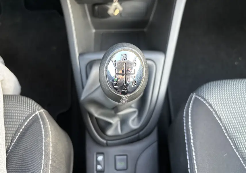 Gros plan sur le levier de vitesses manuel de la Renault Clio IV gris, entouré des sièges avant en tissu gris.