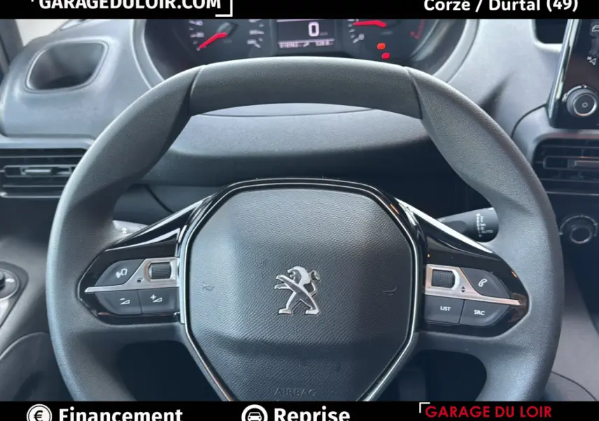 Vue rapprochée du volant noir du Peugeot Rifter 2024 avec commandes intégrées et tableau de bord digital en arrière-plan.