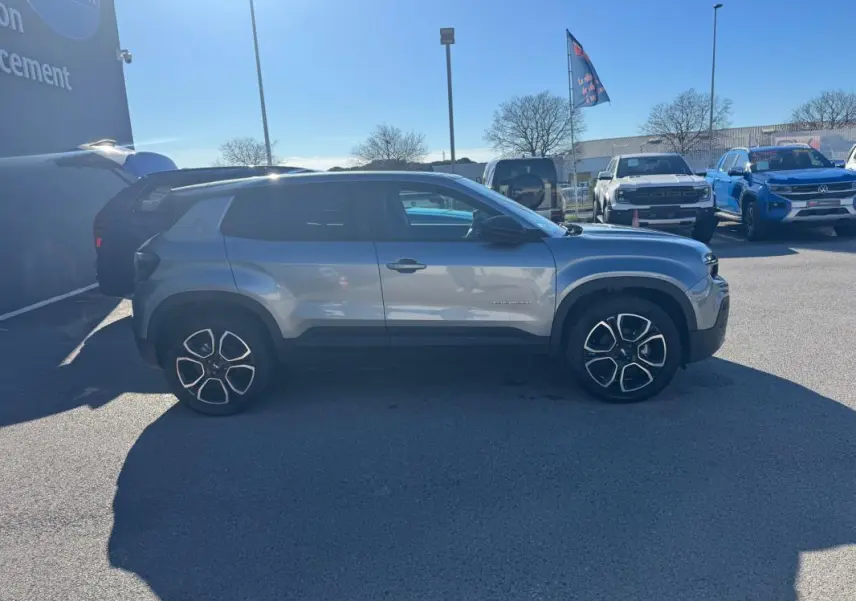 Profil côté gauche d’un Jeep Avenger gris 2025 avec jantes alliage 18 pouces sur parking extérieur.