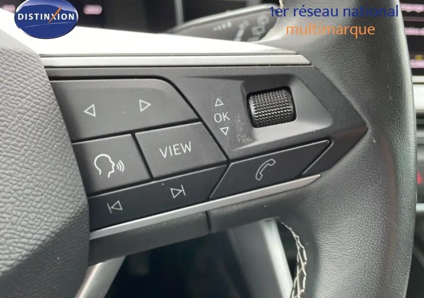 Gros plan sur les commandes multifonctions à gauche du volant en cuir noir du SEAT LEON ST bleu Fjord 2025.