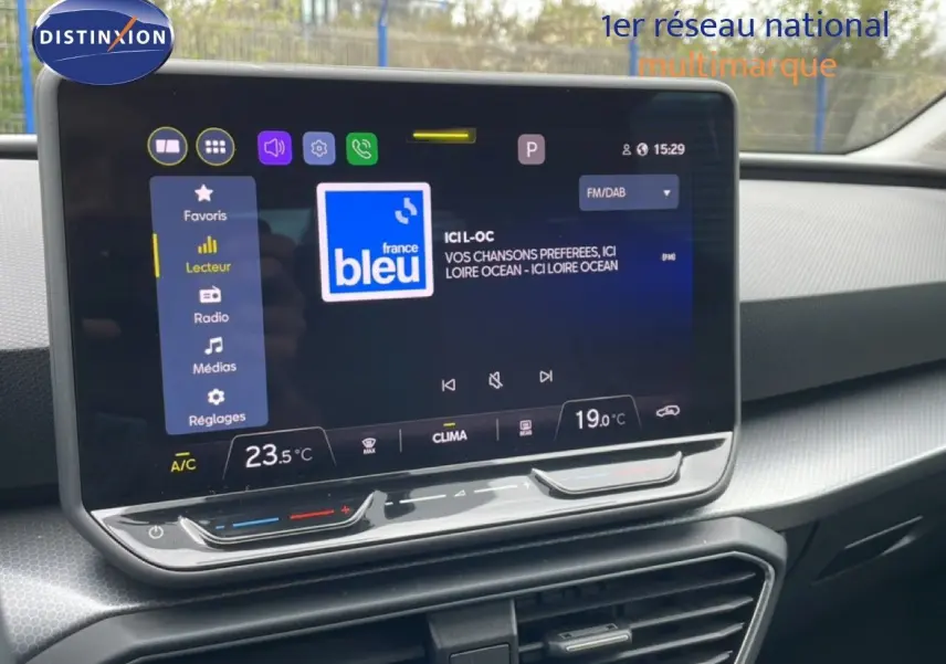 Vue rapprochée de l’écran tactile central du SEAT LEON ST bleu Fjord, affichant la radio France Bleu et la climatisation.