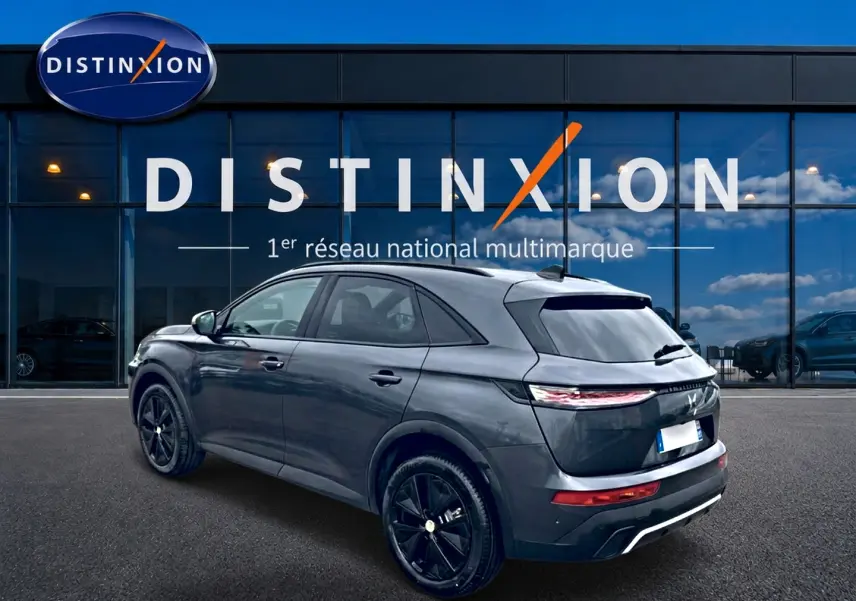 Vue 3/4 arrière droite du DS7 gris titane avec jantes noires, garé devant une vitrine Distinxion.