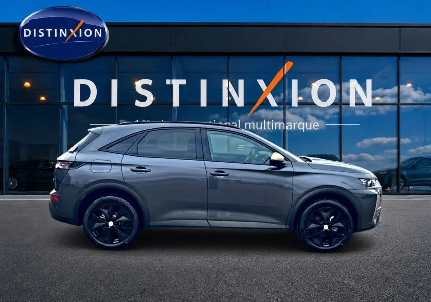 Vue latérale droite d'un DS7 gris titane avec jantes noires, devant une vitrine Distinxion multimarque.