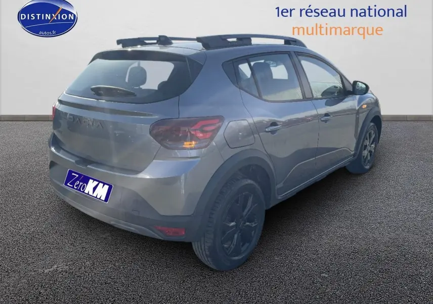 Vue 3/4 arrière droit d'une Dacia Sandero gris schiste avec barres de toit et jantes alu noires.