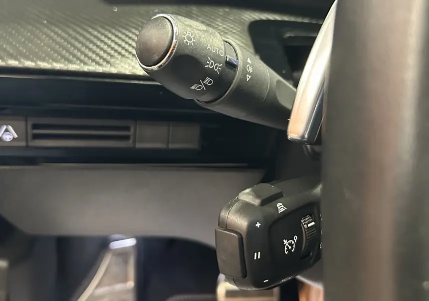 Gros plan sur les commandes au volant du Peugeot 508 SW 2024, soulignant les réglages des phares et du régulateur de vitesse.