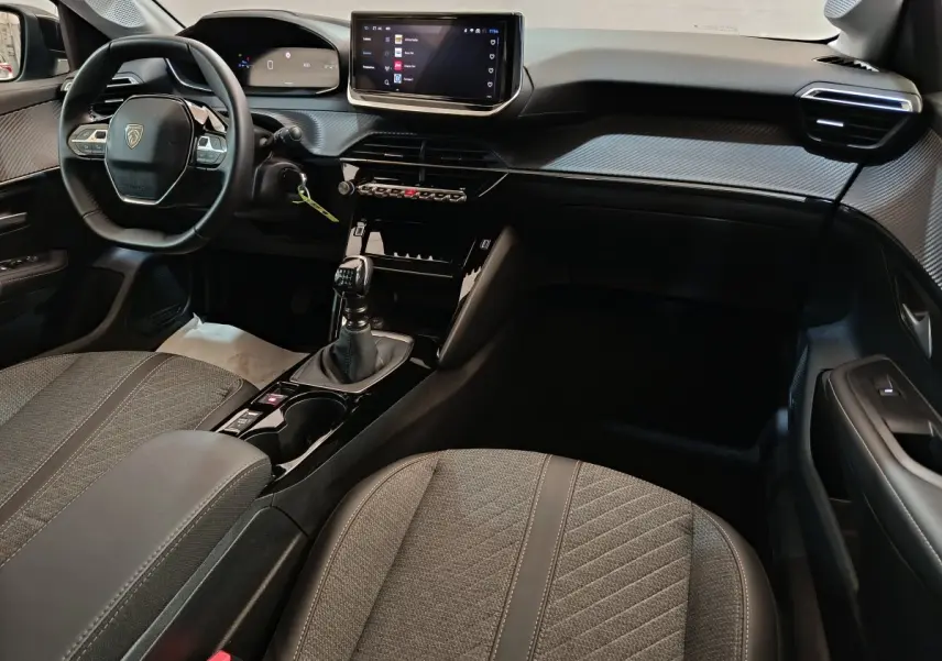 Intérieur de la Peugeot 208 PureTech 100 S&S Allure 2025 en gris, vue côté conducteur avec tableau de bord et écran tactile central.