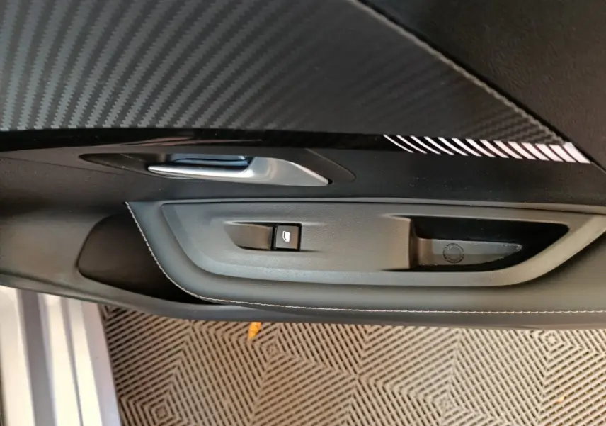 Poignée de porte intérieure côté gauche avec bouton de commande de vitre sur Peugeot 208 gris clair 2025.