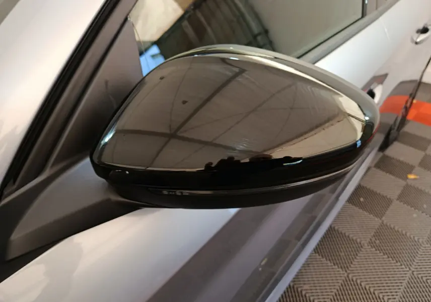 Rétroviseur noir brillant côté gauche d'une Peugeot 208 gris clair, vue rapprochée en intérieur.