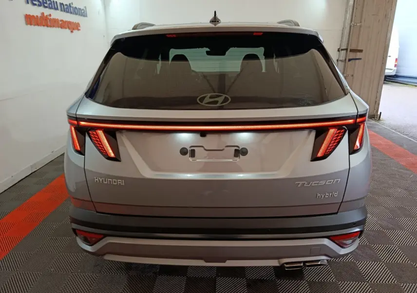Vue arrière d’un Hyundai Tucson 1.6 Hybrid gris clair 2025 avec feux LED distinctifs et double sortie d’échappement.