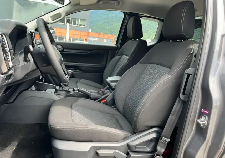 Vue intérieure côté conducteur du Ford Ranger gris carbone 2025, sièges tissu avec accoudoir central et volant multifonctions.