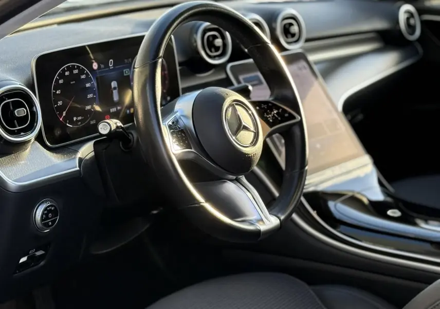 Gros plan sur le volant et la portière côté gauche d'une Mercedes Classe C Break argent avec commandes au volant et finitions noires brillantes.