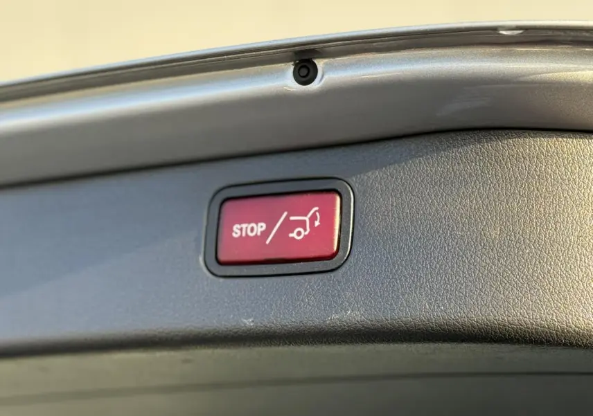 Bouton rouge stop pour fermeture électrique du hayon, visible sur le bord intérieur du coffre d'un Mercedes Classe C Break argent High-Tech.