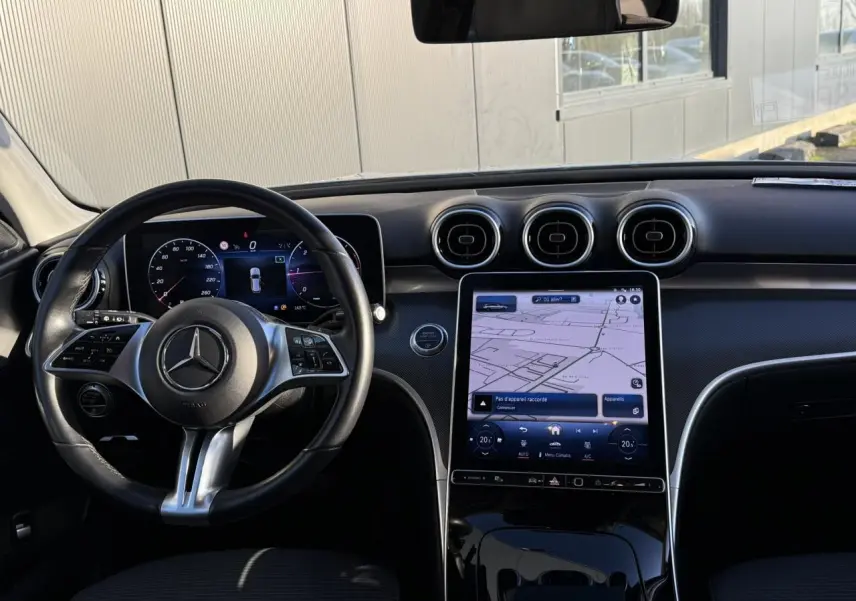 Vue intérieure côté conducteur du Mercedes Classe C Break argent, avec volant cuir et écran tactile de navigation.