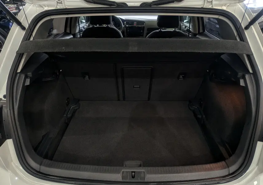 Coffre ouvert d'une Volkswagen Golf VII TSI 125 ch Sound blanc pur, vue arrière montrant l'intérieur spacieux et la banquette arrière.