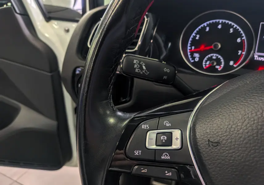 Gros plan sur le volant noir de la Volkswagen Golf VII TSI 125 CH Sound, avec tableau de bord et portière blanche en arrière-plan.