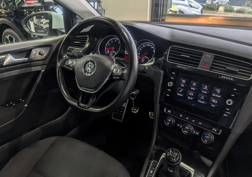 Vue intérieure côté conducteur d'une Volkswagen Golf VII blanche, avec volant multifonction et boîte manuelle six vitesses.