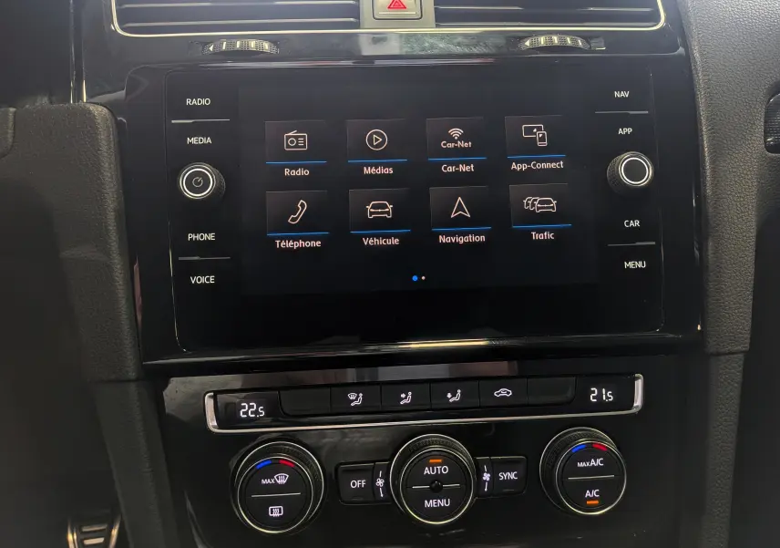 Vue rapprochée de l'écran tactile et de la console de climatisation d'une Volkswagen Golf VII blanche, intérieur noir.