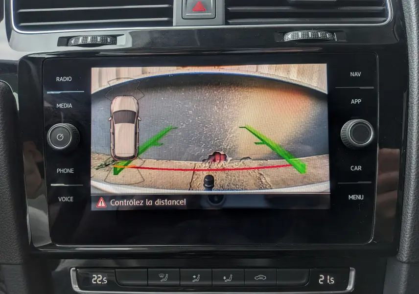 Affichage de la caméra de recul sur l'écran central de la Volkswagen Golf VII blanche, avec guidage vert et rouge et avertissement de distance.