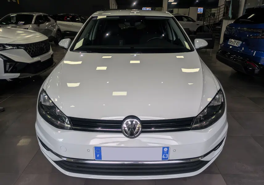 Vue avant d'une Volkswagen Golf VII TSI 125 CH Sound blanche Pure exposée en showroom avec éclairage intérieur.