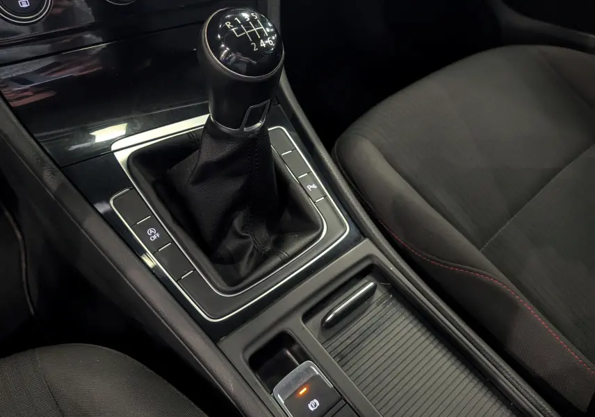 Gros plan sur la console centrale de la Volkswagen Golf VII TSI 125 CH Sound avec levier de vitesse manuel et sièges tissu noirs.