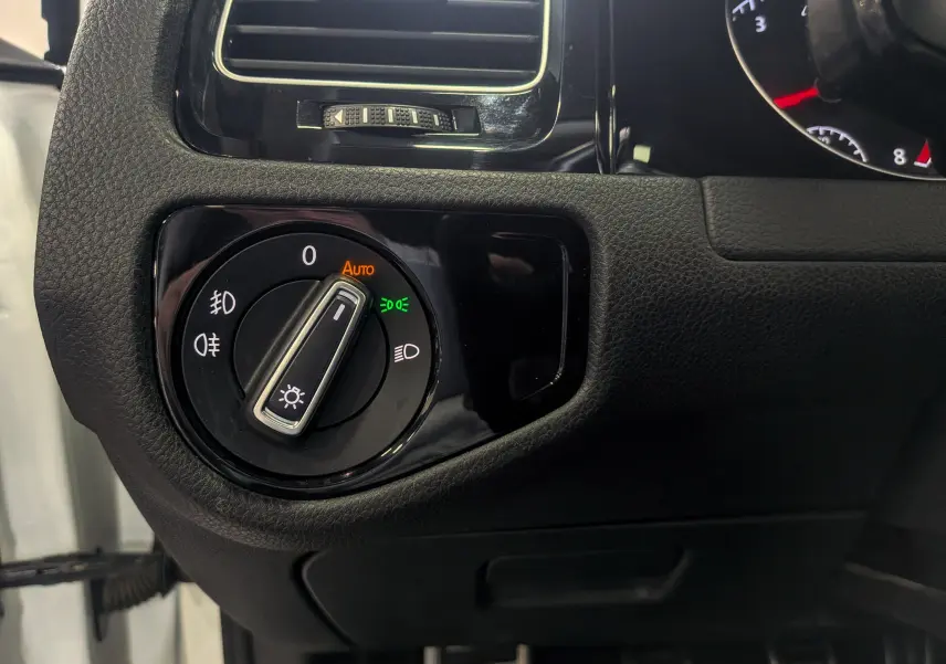 Gros plan sur le bouton de commande des phares dans l'habitacle noir d'une Volkswagen Golf VII blanche.