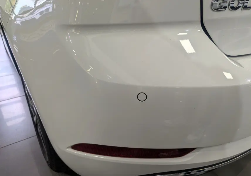 Gros plan sur l'angle arrière gauche d'une Volkswagen Golf VII TSI blanche, avec feu arrière et capteur de recul visibles.