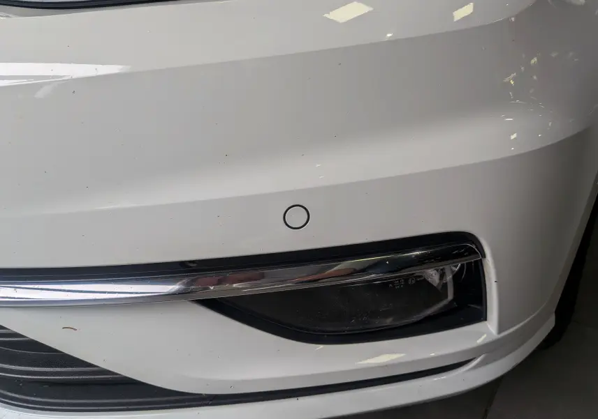 Gros plan sur le pare-chocs avant blanc pur d'une Volkswagen Golf VII TSI 125 CH avec antibrouillard et capteur de stationnement.