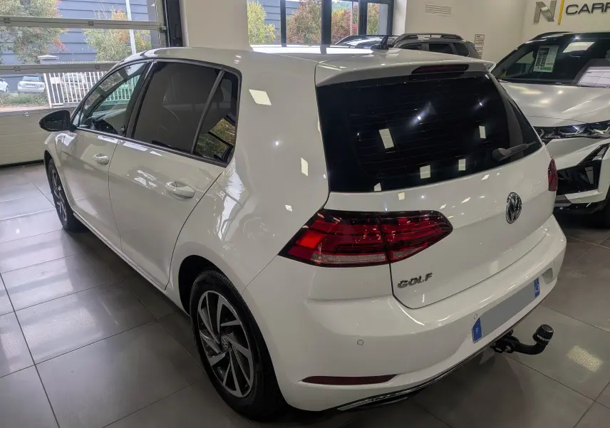 Vue 3/4 arrière droite d'une Volkswagen Golf blanche Pure avec hayon et attelage en showroom.
