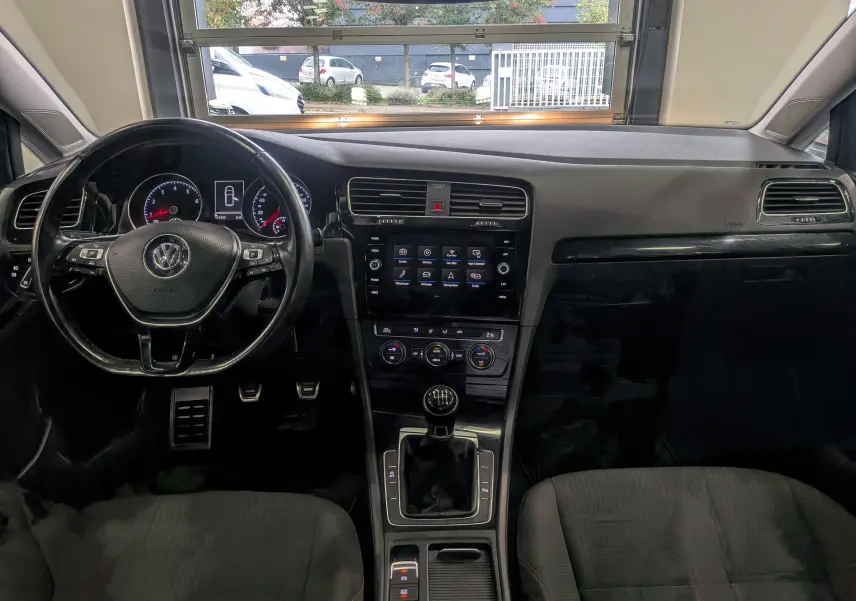 Vue intérieure avant de la Volkswagen Golf VII TSI 125 CH Sound 2018, tableau de bord noir avec volant multifonction et boîte manuelle.