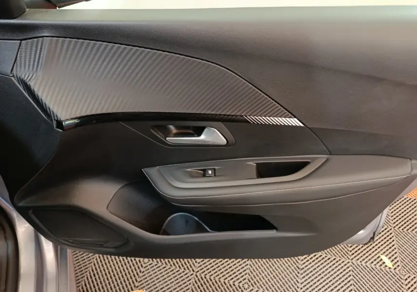 Vue côté gauche de la porte intérieure noire avec insert effet carbone d'une Peugeot 208 gris clair 2025.
