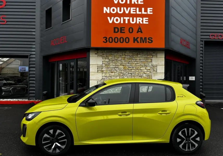 Peugeot 208 Hybrid jaune vue de profil côté gauche, avec jantes noires et toit noir, devant un bâtiment commercial.