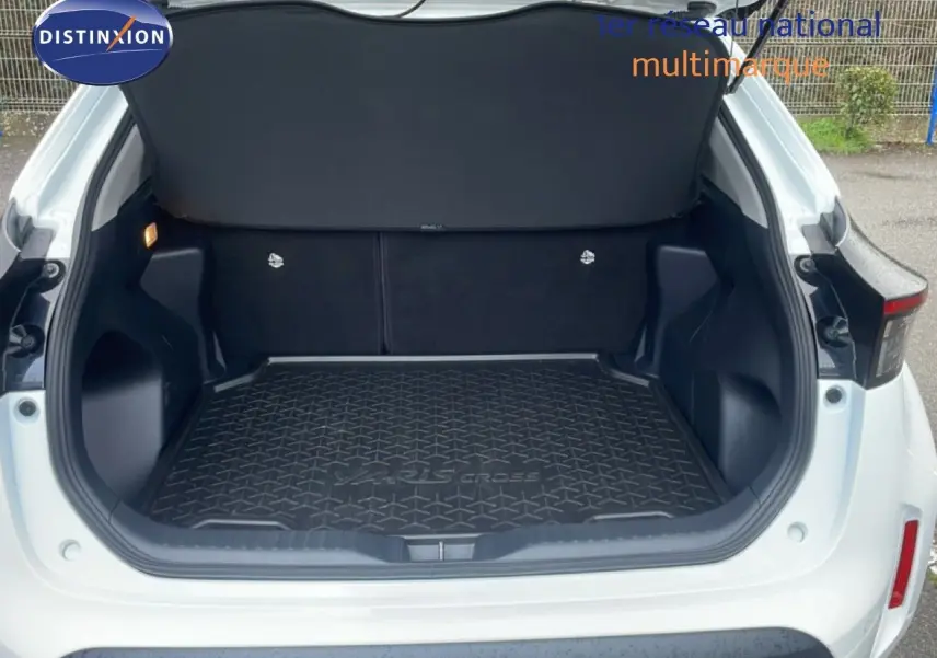 Coffre ouvert vu de l'arrière d'une Toyota Yaris Cross blanche 2024, avec tapis de coffre noir marqué "Yaris Cross".
